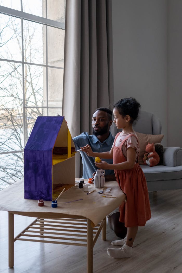 Crafting Captivating Headlines: Your awesome post title goes here A father and daughter enjoy painting a dollhouse indoors, spending quality family time together.