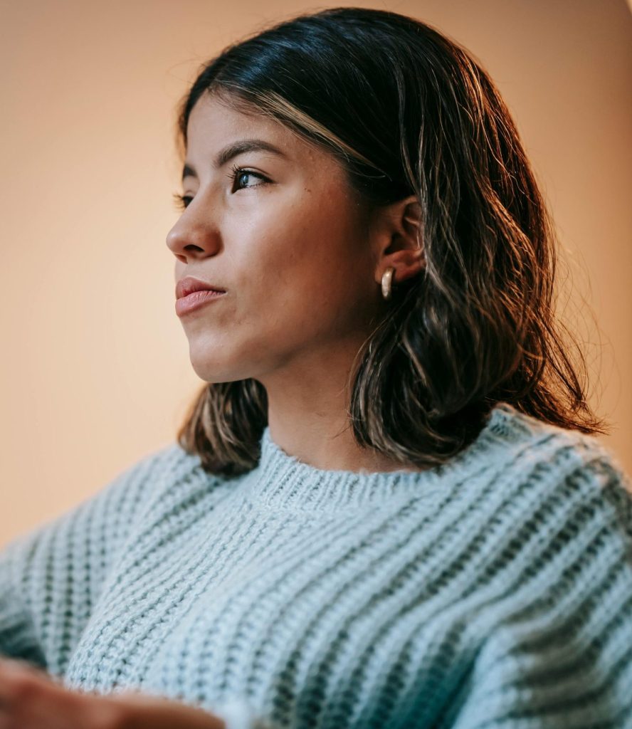 Low angle of pensive Asian female in knitted sweater reading magazine and thoughtfully looking away