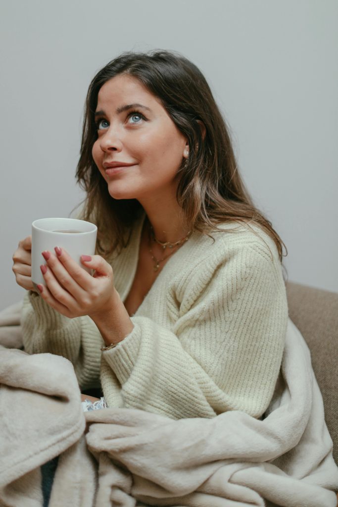 Woman enjoying a cozy moment indoors with a warm mug, wrapped in a blanket.