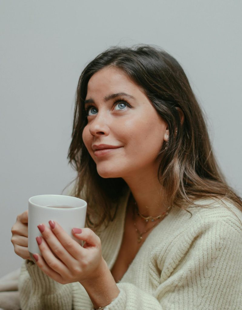 Woman enjoying a cozy moment indoors with a warm mug, wrapped in a blanket.